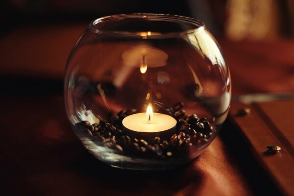 A candle in a jar with coffee on the table