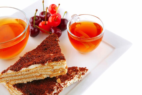 Tasses de thé, morceaux de gâteau, cerise sur un plateau blanc