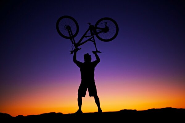 Uomo sollevato bicicletta sullo sfondo del tramonto, bel cielo