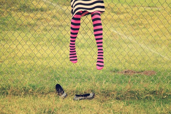 A girl in pink striped leggings jumps at the fence