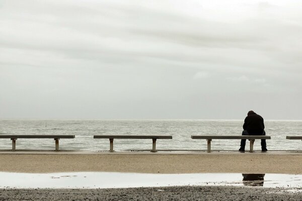 A man sitting alone on the seashore on a bench