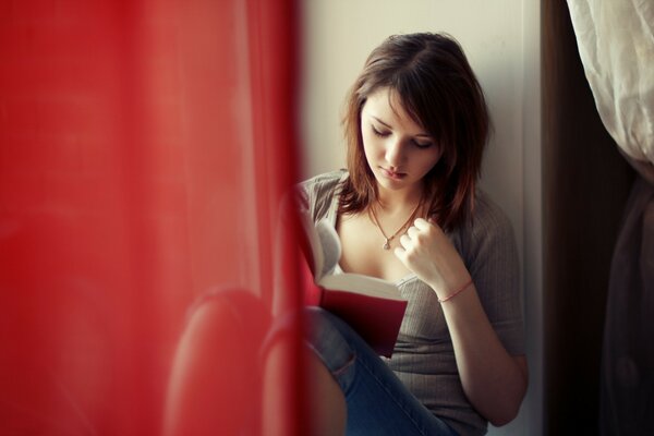 The girl sitting at the window is intently reading a book