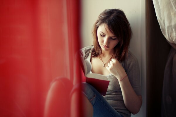 Dziewczyna siedząca przy oknie koncentruje się na czytaniu książki