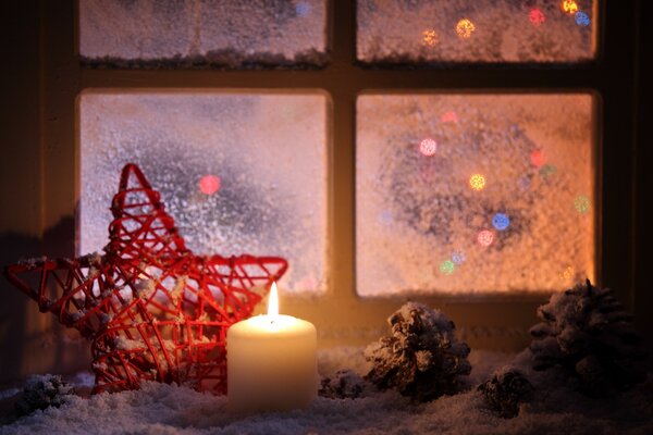 A red star and a candle on the background of the window