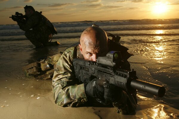 A soldier with a gun on the seashore at sunset
