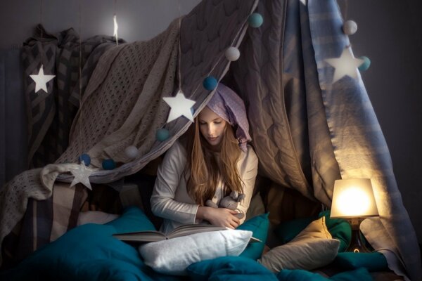 The girl is sitting on the bed with a book