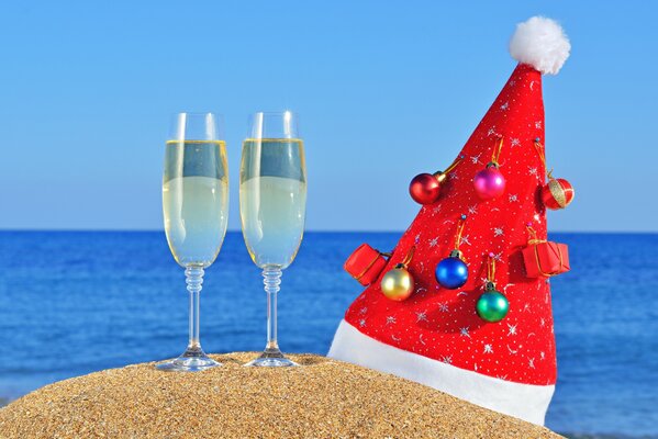 Cappello di Natale con bicchieri di champagne sulla sabbia