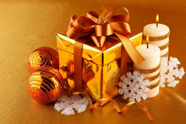 Prezent na Boże Narodzenie w złotym pudełku ze wstążką. Świece noworoczne na żółtym tle