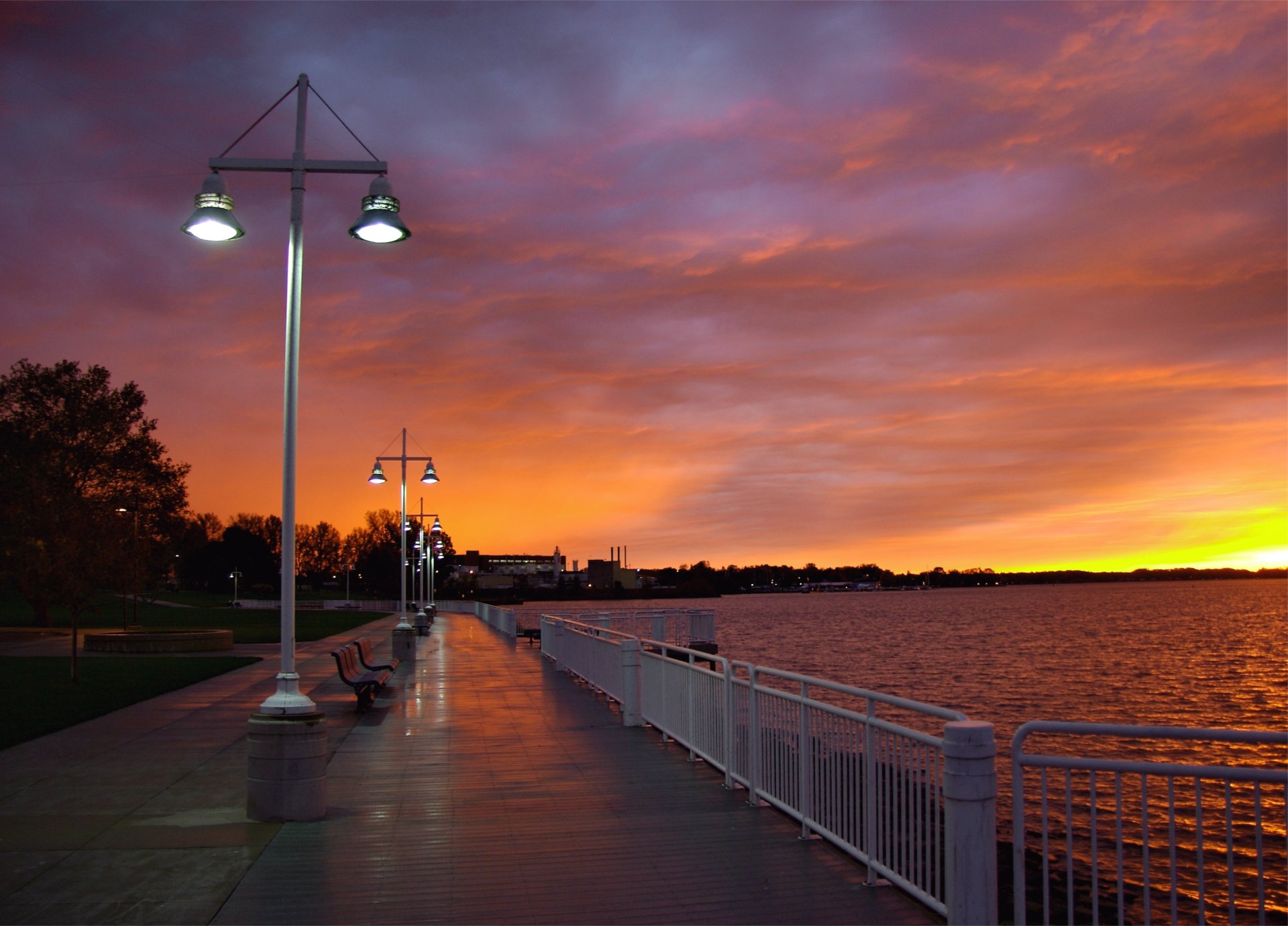 ciudad tarde puesta de sol cielo nubes nubes terraplén árboles bancos río linternas luz