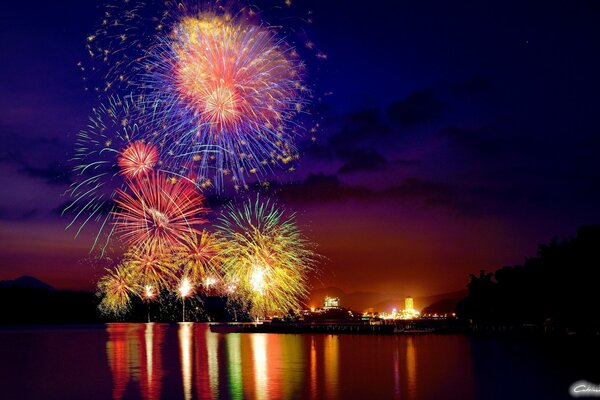 Gorgeous fireworks over the city and colorful reflections of the city on the smooth surface of the water