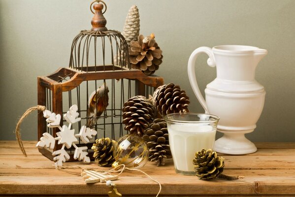 Oiseau dans une vieille cage entourée de cônes, flocons de neige et un verre de lait