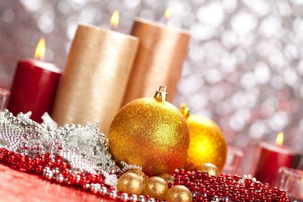 Lit candles and golden Christmas balls lying on a table strewn with beads