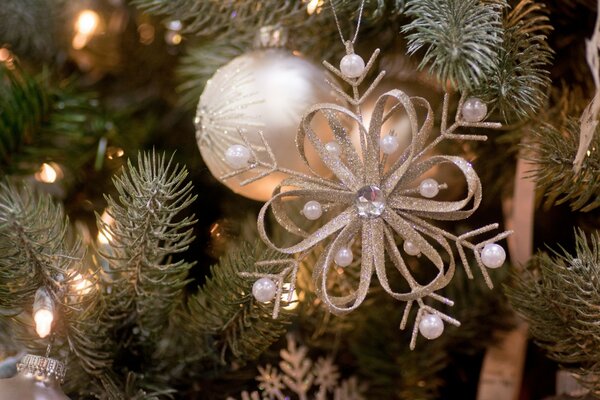 A flower with beads and a ball on a Christmas tree illuminated by lights