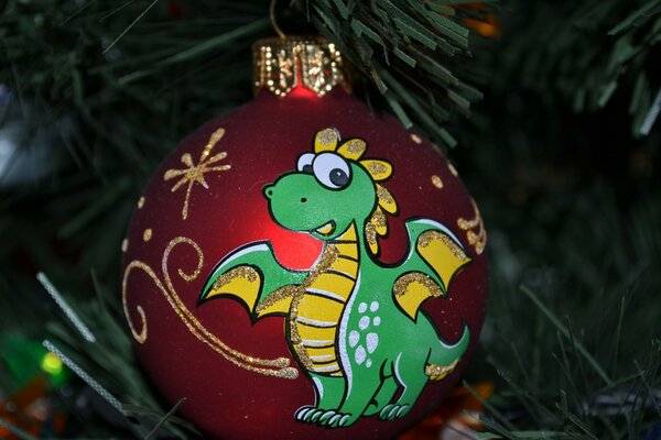 Boule rouge de Noël avec dragon vert dessiné sur fond de branches vertes artificielles de sapin de Noël