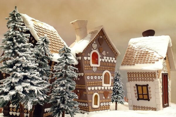 Casas de pan de jengibre de juguete y árboles de Navidad cubiertos de nieve en mí sobre un fondo beige