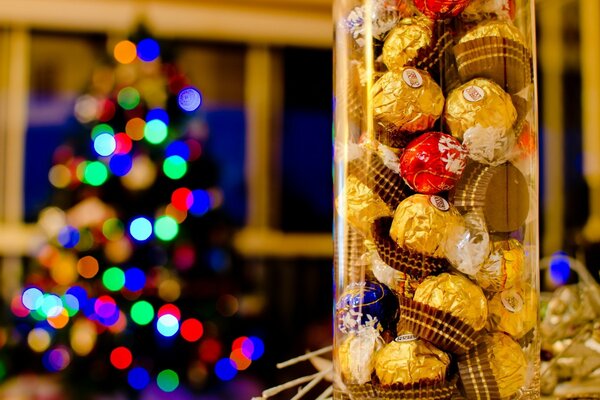 Ein Glas mit Süßigkeiten im Vordergrund und ein geschmückter Weihnachtsbaum auf der Rückseite