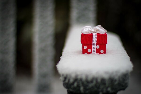 Un piccolo regalo carino su un negozio coperto di neve nel parco. Scatola regalo rossa