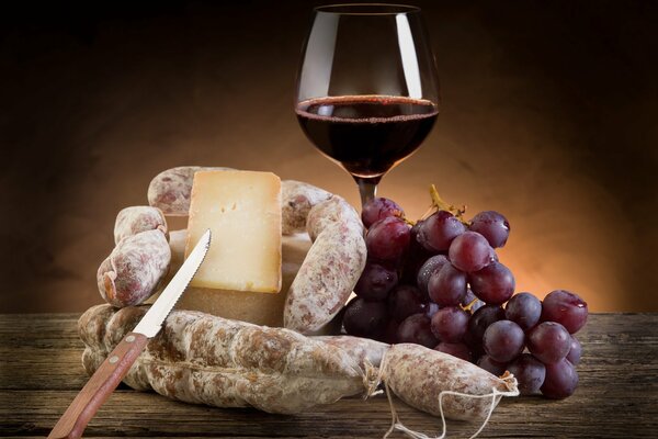 Красное вино в бокале с закуской из сыра, колбасы и винограда