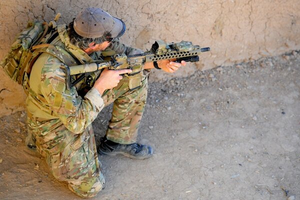 Un soldado en camuflaje se agacha y apunta con un rifle