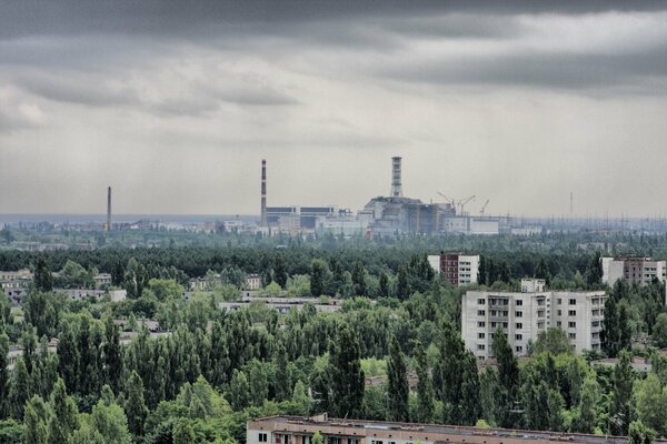 Città di Pripyat, case tra gli alberi, impianto tubo lontano e cielo nuvoloso