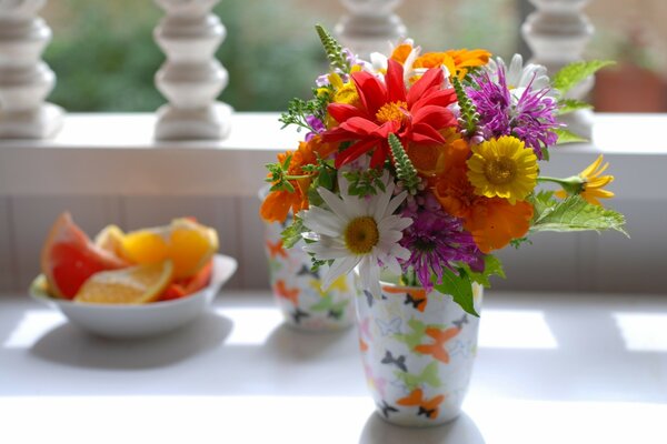 Mazzo di fiori in un bicchiere su una terrazza bianca e un piattino con frutta tagliata