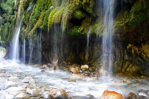 Ein Mann steht unter einem Wasserfall in Griechenland