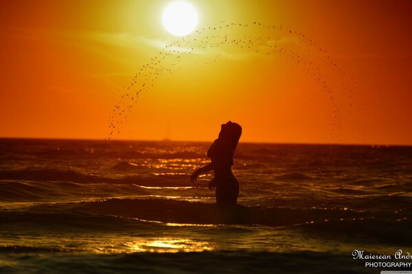 Chica en el agua en el fondo de la puesta de sol