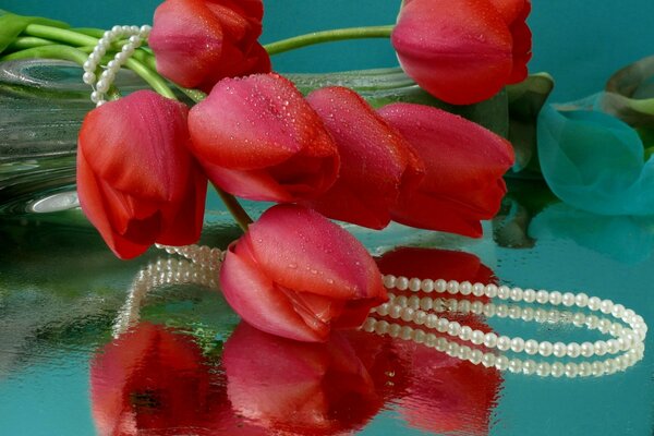 Tulipanes rojos envueltos en un collar de perlas se encuentran en una mesa brillante