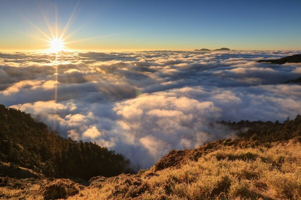 The sun shines over clouds and mountains
