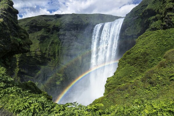 Cascada y arco iris entre las montañas verdes