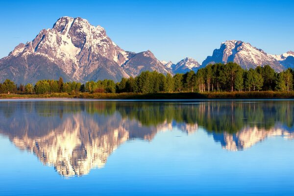 Lago azul con superficie de espejo en el fondo de las montañas