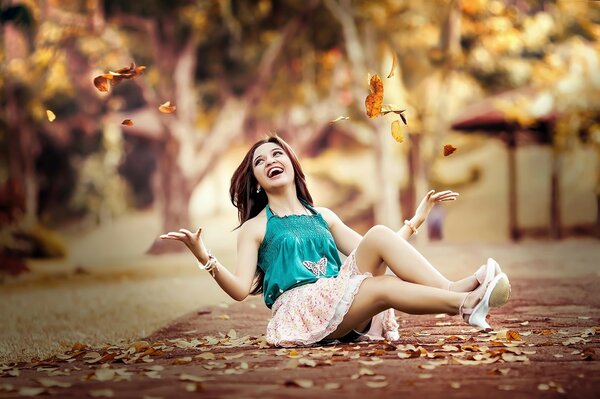 Young girl tosses leaves sitting on the ground in the park