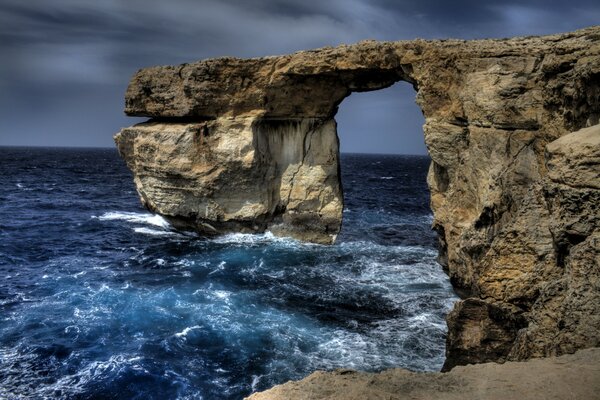 An arch of rocks in the blue sea, waves beating against the rocks