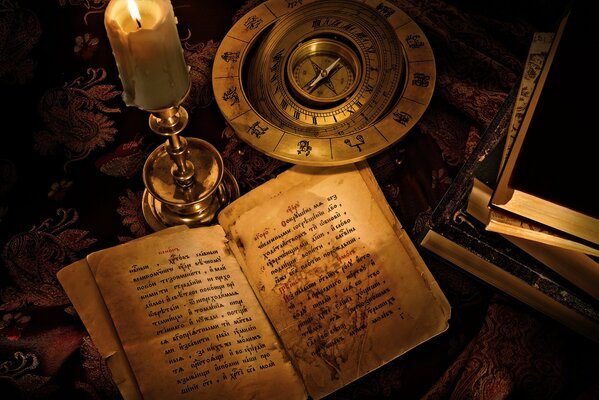 Zodiac signs. A candle on the table. An open book. Antique compass