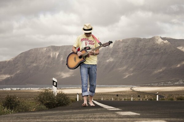 Guy guitariste marchant sur la route sur fond de montagnes