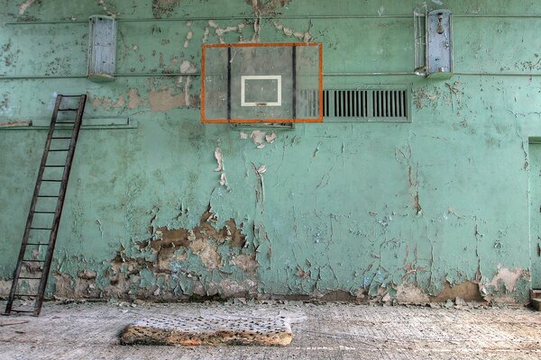 Заброшенный спортзал, стена в облупленной краске, сгнивший мат на полу