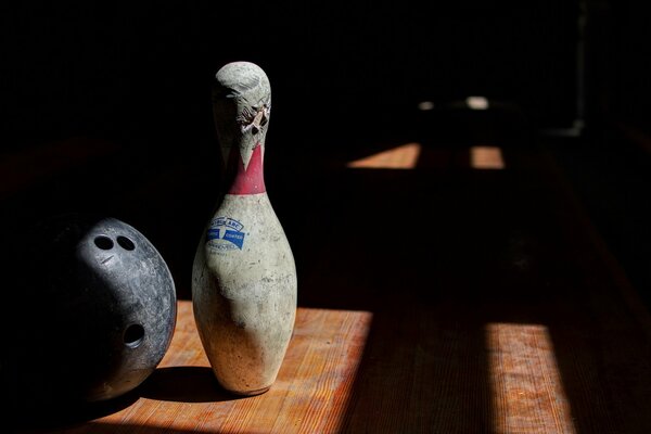 Una stanza buia, una luce dalla finestra illumina la palla e il birillo da bowling