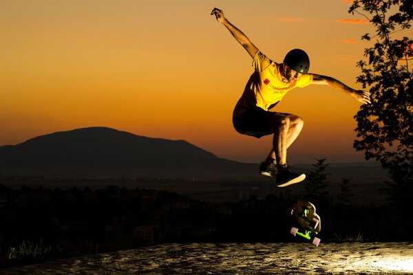 A skateboarder in a yellow T-shirt and a black helmet against the background of the evening sky