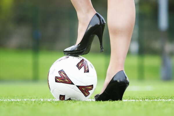 Женские ноги на каблуках на футбольном мяче