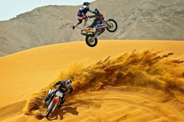 Motorcycles ride through the desert, raising sand