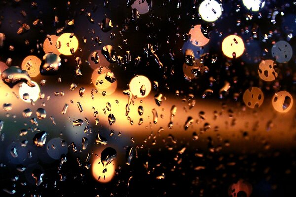 Lumières de nuit translucides à travers le verre dans les gouttes de pluie