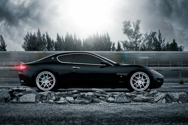 Black maserati rides under the rays of the sun