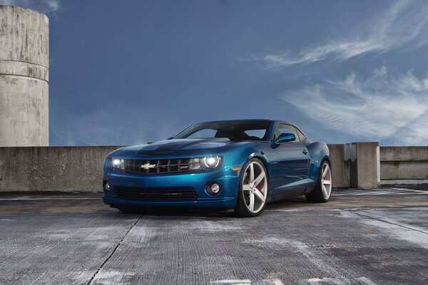 Bleu chevrolet camaro se trouve dans un parking sur fond de beau ciel