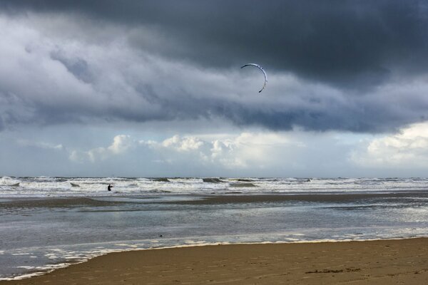 Ein Kite-Surfer übt seine Fähigkeiten in den Wellen eines unruhigen Meeres vor dem Hintergrund eines Gewitterhimmels aus