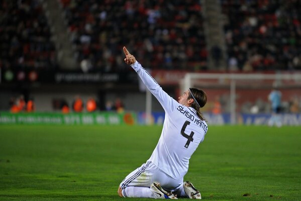 Sergio Ramos sits on the football field and points up with his hand