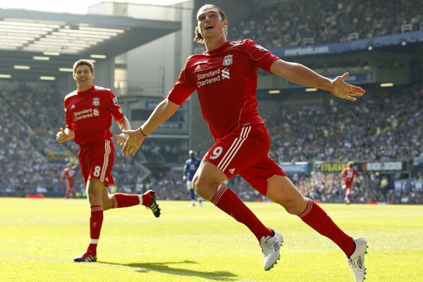 Two Liverpool football players happily run across the field