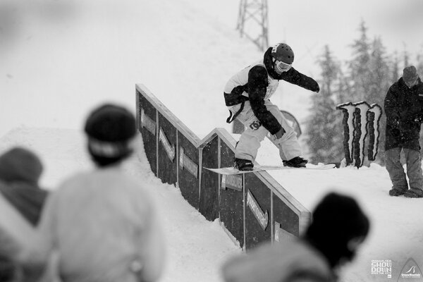 Snowboarder roule sur une planche sur une clôture étroite devant les spectateurs