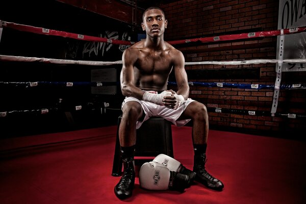 A black athlete is sitting on a chair in the ring