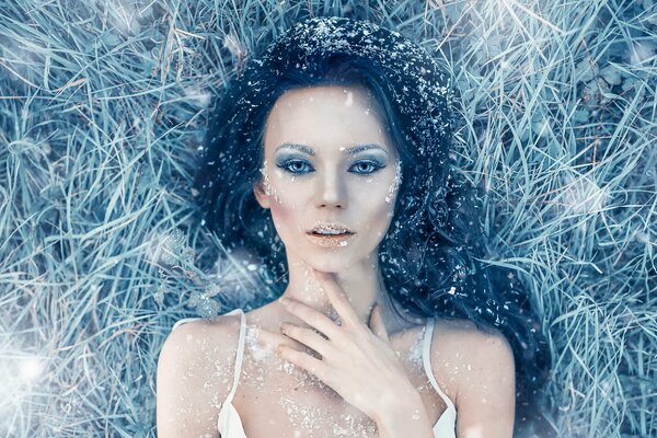 Девушка в морозной траве с морозным макияжем покрытая инеем