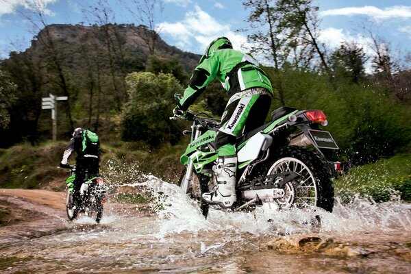 Deux motocyclistes en noir et vert se déplacent dans un ruisseau de montagne